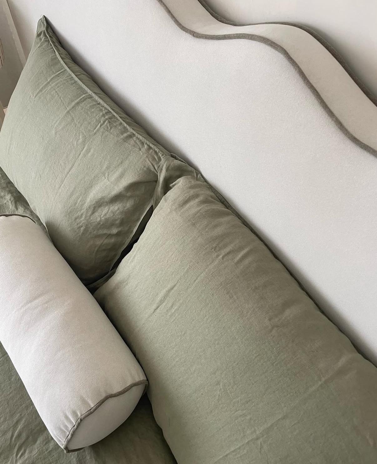 Detalle cenital de almohadones de lino verde salvia y almohadón cilíndrico sobre respaldo ondulado